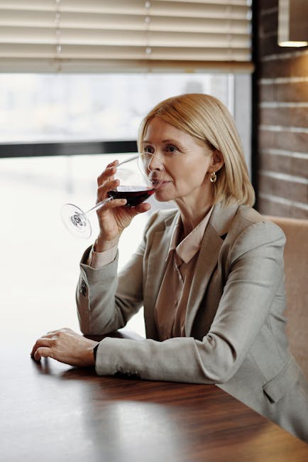 Mature woman in business attire sipping wine at a café during the day.
