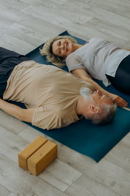Elderly couple lying on yoga mats, smiling and enjoying relaxation indoors.
