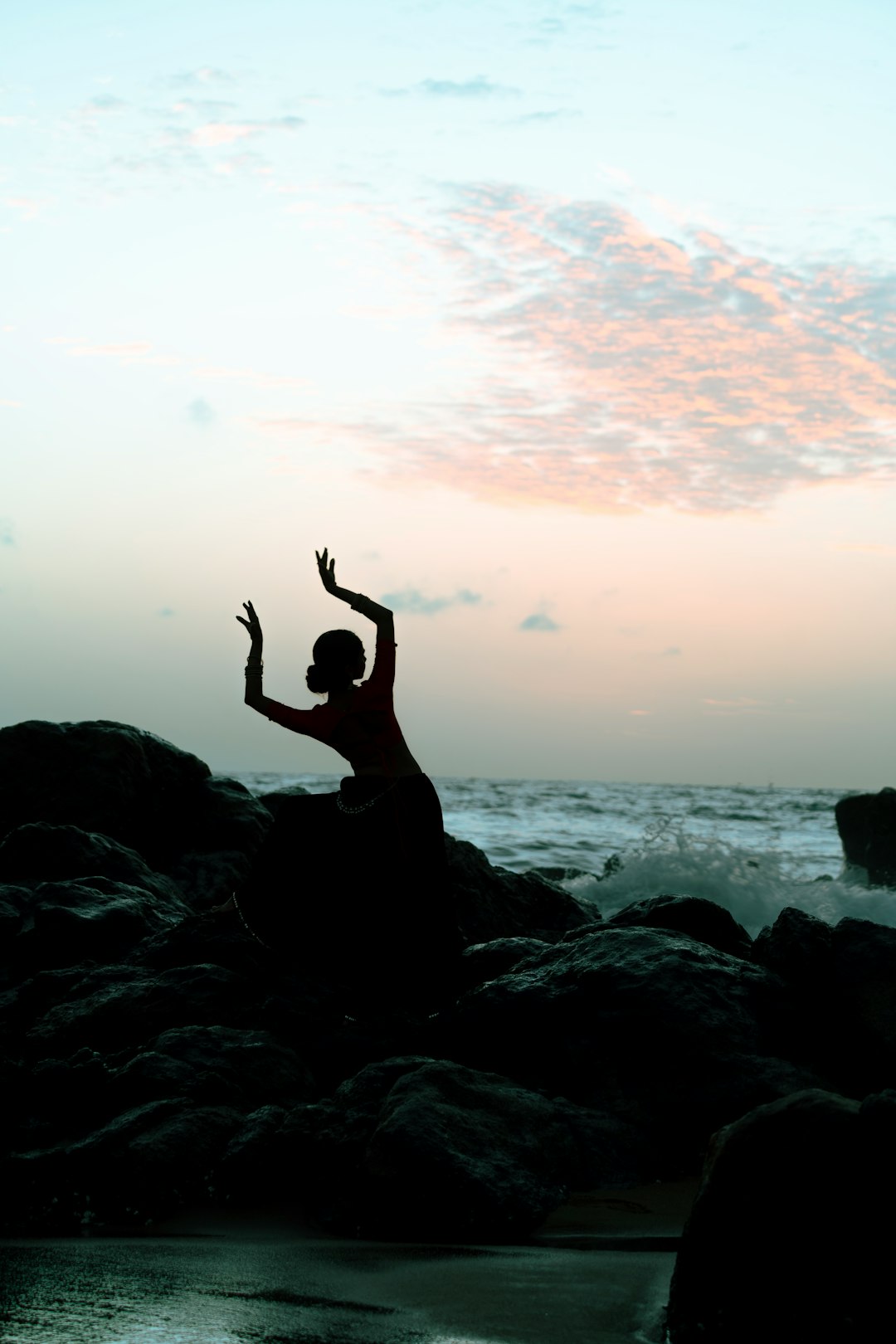A silhouette dances atop the rocky shore.