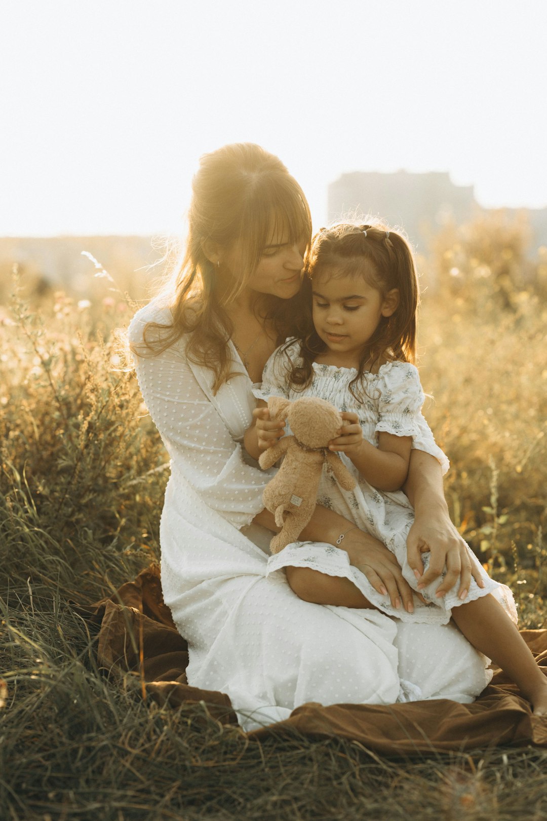 A woman and a little girl sitting on a blanket in a field
