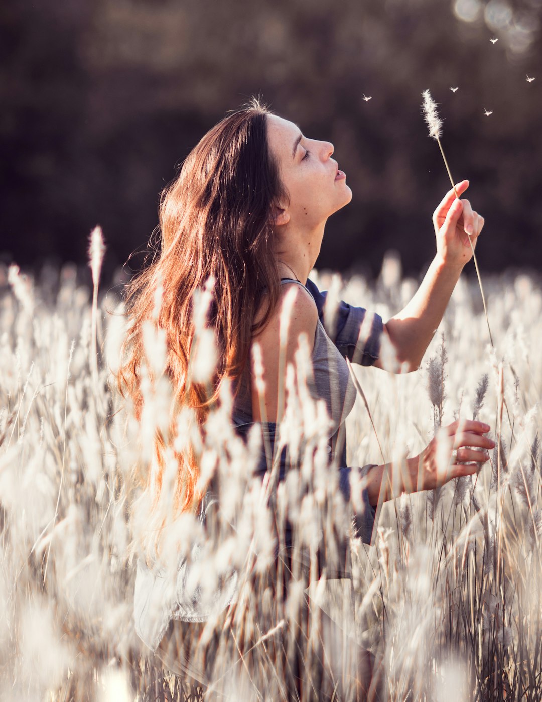 woman blowing white flower in the middle of field