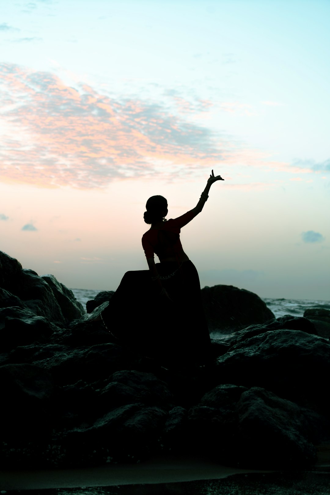 A silhouetted dancer poses beside rocky waters.