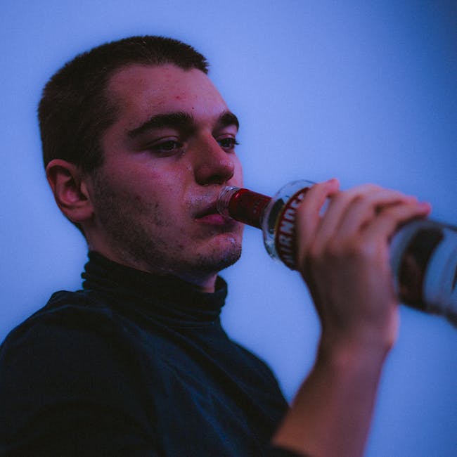 Portrait of a young man drinking from a vodka bottle, suggesting contemplation or depression.